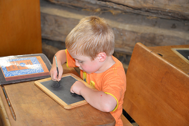 Boy writing on slate in the Carver County Historical Society log granary at the Carver County Fair