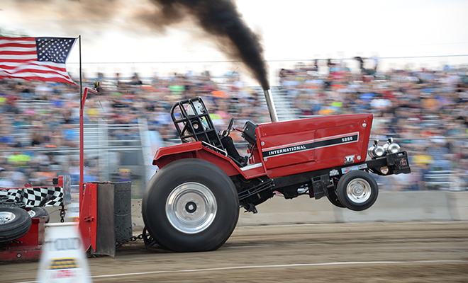 a red International tractor's wheels leave the ground in the NTPA tractor pull at the Carver County Fair