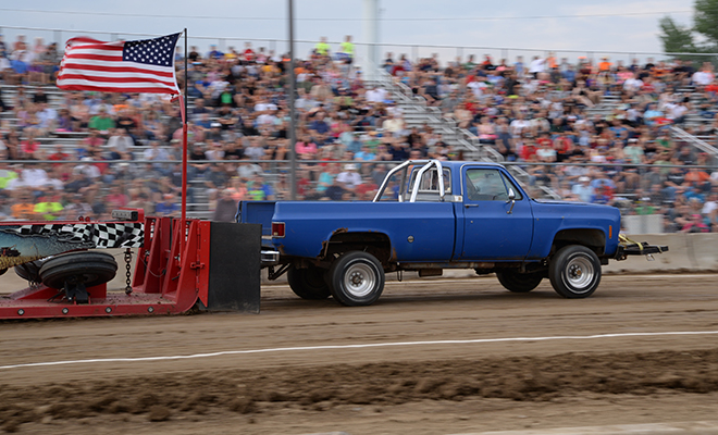 a blue pickup truck pulls a weighted sled at the Carver County Fair Out-of-Field Truck Pull