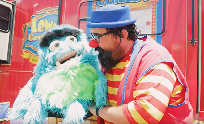 Lew-E the clown talks to a large blue and green furry puppet
