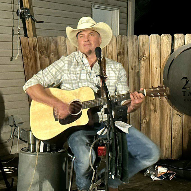 Grady Kruse performing on a patio with a microphone and acoustic guitar