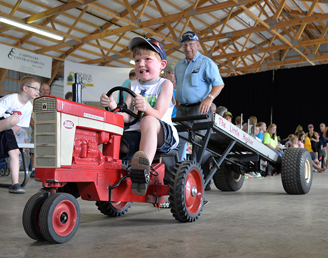 a boy pedaling a miniature tractor in the Kids' Pedal Tractor Pull at the Carver County Fair